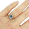 Oval teal sapphire solitaire with a halo of diamonds, hammered gold ring on hand