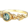 a side view of a golden leaves ring with accent diamonds and green sapphire