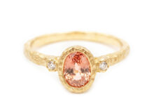 Alternative engagement ring with an oval peach sapphire and two diamonds